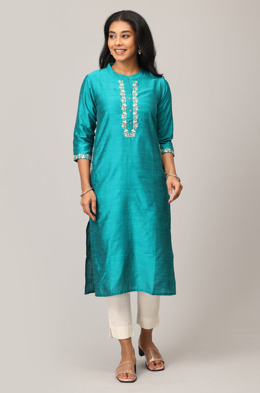 Woman wearing a teal kurta with white embroidery on a plain background